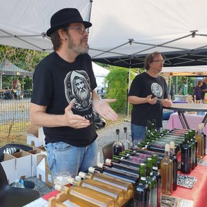Deux exposants discutent derrière un étal de bouteilles sous un chapiteau.