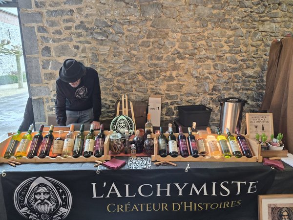 Stands de L'Alchymiste : bouteilles de liqueurs alignées, vendeur penché, mur de pierre.