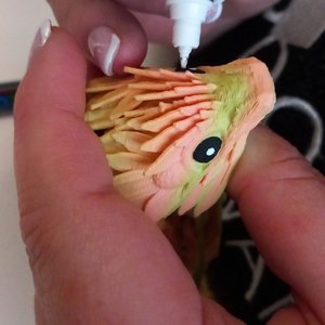 Main féminine peignant un petit oiseau en papier coloré, détail des plumes.