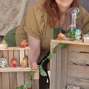 Vendeuse souriante présentant des figurines artisanales colorées sur étagères rustiques.