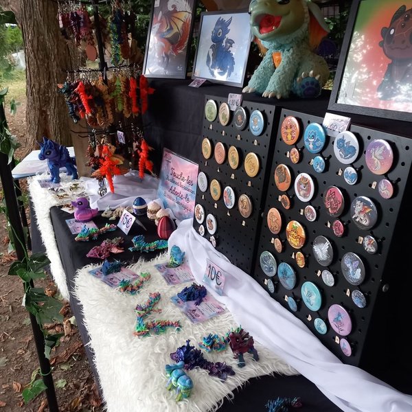 Stands de badges, peluches et bijoux fantaisie colorés sous une tente, décor féerique.
