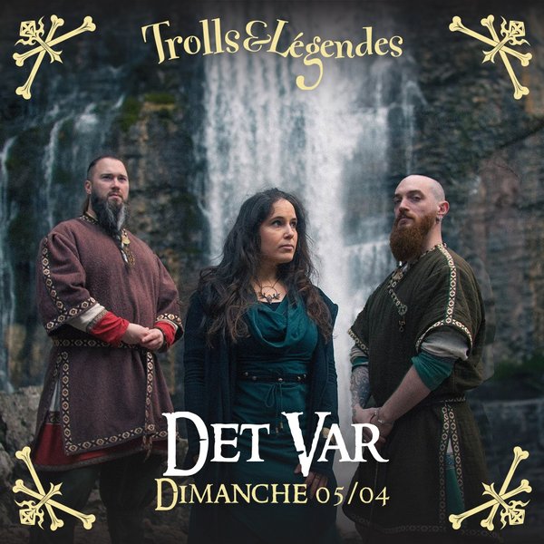 Det Var - Trois personnages en costumes médiévaux se tiennent devant une cascade. L'homme à gauche porte un vêtement rouge orné. La femme au centre, vêtue de bleu et de noir, regarde intensément. L'homme à droite a une barbe et un habit vert.