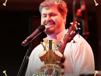 One Shot Bards - Un artiste souriant chante sur scène lors de l'événement Trolls & Légendes. Il porte une chemise blanche et est équipé d'un microphone et d'un instrument. Le design en arrière-plan indique "One Shot Bards" et la date, samedi 04/04.