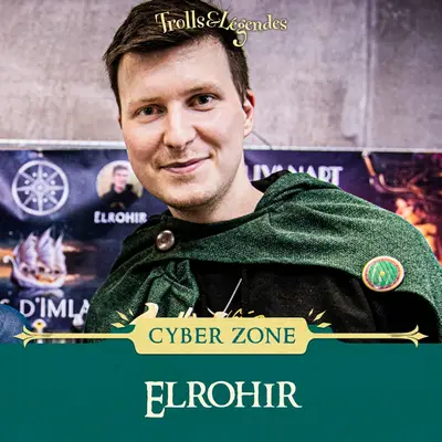 Elrohir - Homme souriant portant une cape verte, avec un fond de salon et le logo de Trolls & Légendes.