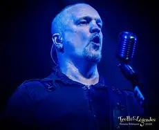 MANEGARN en live sur la scène bleue: portrait serré d’un chanteur concentré, micro à la main, oreillette et chemise sombre. L’atmosphère est électrique et sombre, typique d’un show de concerts au Festival 2026.