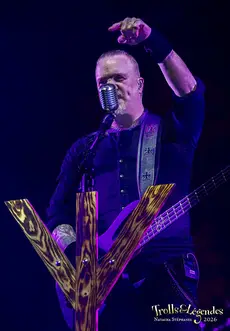 MANEGARN sur scène lors d’un concert au Festival 2026. Il chante dans un micro vintage, veste sombre et guitare électrique, bras levés en geste d’emportement. Devant lui, une décoration en bois en forme de V; ambiance bleu nuit. Hub: Concerts.