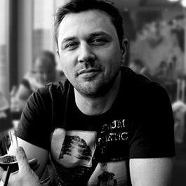 Sylvain CORDURIE - Un homme souriant dans un café moderne en noir et blanc.