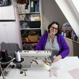 Femme souriante à une machine à coudre, atelier créatif avec tissus et bobines.