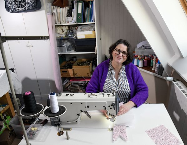 Femme souriante à une machine à coudre, atelier créatif avec tissus et bobines.