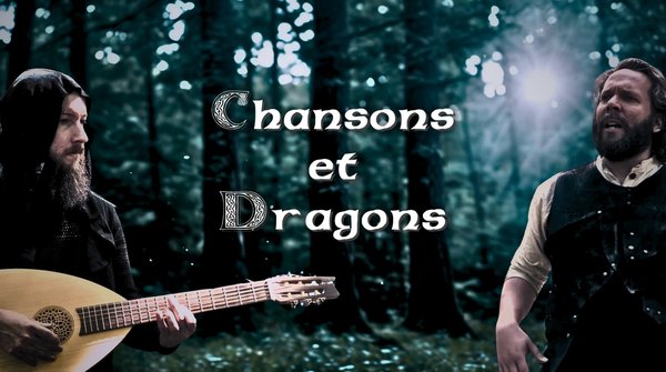 Chansons et Dragons. Deux hommes se tiennent dans une forêt, l'un jouant d'un instrument à cordes, et l'autre chantant. Le premier porte une cape noire et a une barbe, tandis que le second est vêtu d'une chemise claire et d'un gilet sombre.