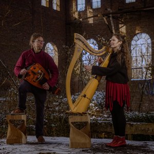 Fyndus. Deux musiciens se produisent dans un ancien bâtiment en ruine, recouvert de neige. L'homme, portant une chemise bordeaux et des lunettes, joue d'un instrument en bois sur une plateforme.