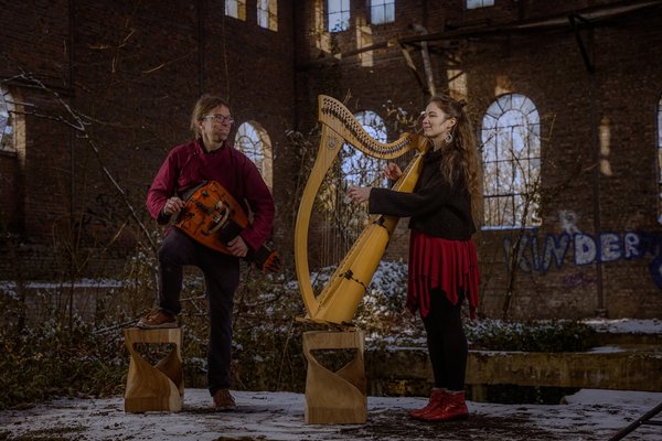 Fyndus. Deux musiciens se produisent dans un ancien bâtiment en ruine, recouvert de neige. L'homme, portant une chemise bordeaux et des lunettes, joue d'un instrument en bois sur une plateforme.