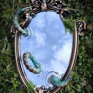 Miroir ancien au sol reflétant le ciel, entouré de mousse et d'un serpent vert fantastique.