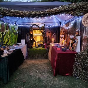 Bannière de stand féerique illuminé aux guirlandes, tables d'artisanat et décor forestier.