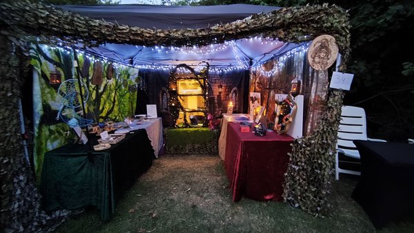 Bannière de stand féerique illuminé aux guirlandes, tables d'artisanat et décor forestier.