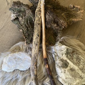 Deux baguettes artisanales en bois posées sur une fourrure, entourées d'écorce et de pierres.