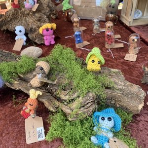 Petits personnages en laine crochetée sur mousse et écorce, décor artisanal coloré.