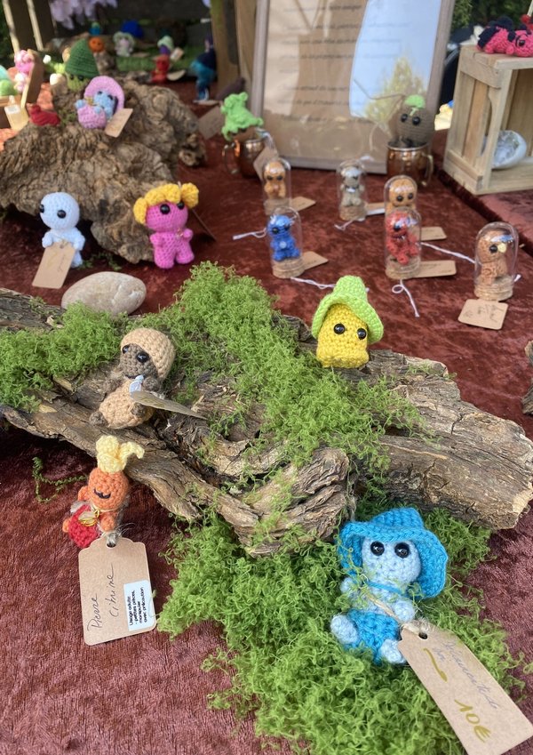 Petits personnages en laine crochetée sur mousse et écorce, décor artisanal coloré.