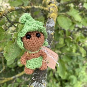 Petit doudou tricoté brun avec bonnet et couche verts accroché sur une branche.