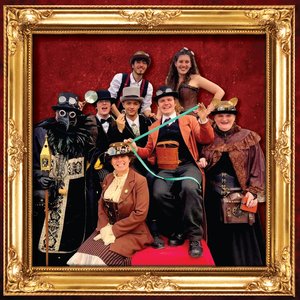 Groupe de personnes déguisées en costumes steampunk, parmi elles, un homme portant un masque de style gaz. Ils posent ensemble en souriant devant un fond rouge, avec un cadre doré autour de l'image.