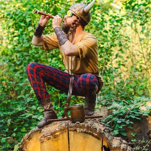 Bardix le Gaulois - Viking moderne jouant de la flûte dans la forêt sur un tronc d'arbre.