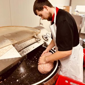 Employé en tablier pressant de la viande hachée dans une grande machine de préparation.