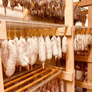 Râtelier de saucissons secs suspendus en rangées sur étagères en bois.
