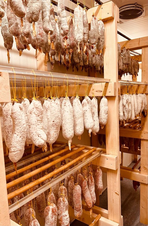 Râtelier de saucissons secs suspendus en rangées sur étagères en bois.