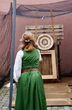 Personnage vêtu de vert lançant une hachette vers une cible en rondins.