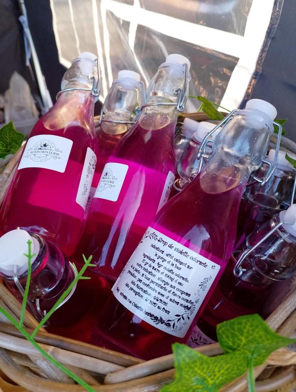 Bouteilles à fermeture mécanique contenant sirop rose vif disposées dans un panier décoré.