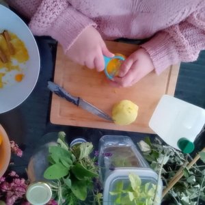 Mains épluchant un fruit jaune sur planche, herbes et ustensiles autour.