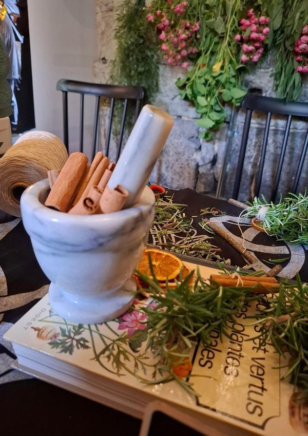 Mortier blanc avec bâtons de cannelle, herbes séchées et fleurs, ambiance atelier magique.