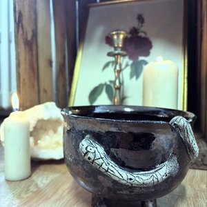 Petit chaudron céramique patiné sur trois pieds, bougies et tableau floral en arrière-plan