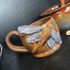 Tasse en céramique brune ornée d'une libellule sculptée en relief.