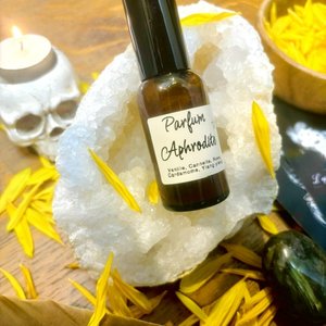 Flacon de parfum "Aphrodite" posé sur une géode blanche, pétales jaunes et bougie skull.