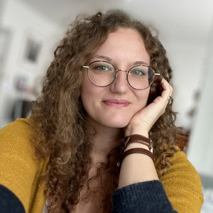 Célia BEAUDUC - Portrait d'une femme souriante avec des lunettes et des cheveux bouclés.
