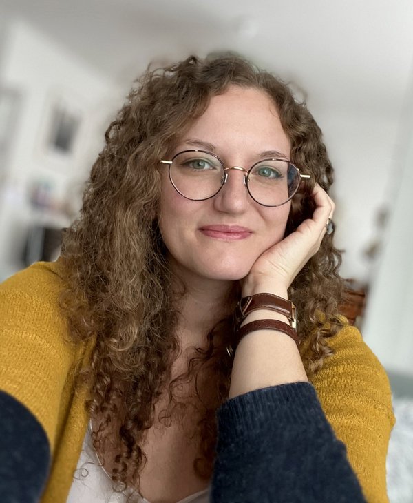 Célia BEAUDUC - Portrait d'une femme souriante avec des lunettes et des cheveux bouclés.