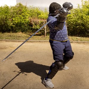 Armeur en tenue d'escrime historique brandissant une épée en plein duel.