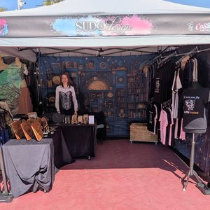 Stand sous tente SUDOdesign vendant T-shirts et objets artisanaux, exposante souriante.