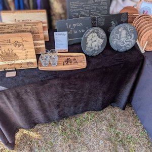Stands de planches et dessous de verre gravés en bois sur une table noire, style médiéval.
