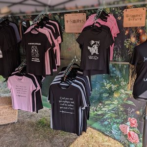Stand de t-shirts noirs et roses à motifs et slogans féeriques au festival Trolls & Légendes