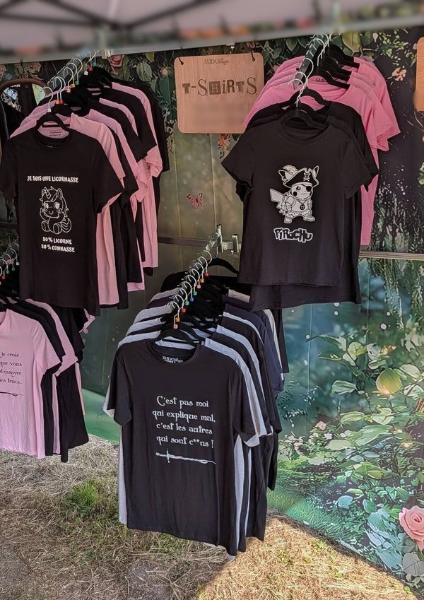 Stand de t-shirts noirs et roses à motifs et slogans féeriques au festival Trolls & Légendes